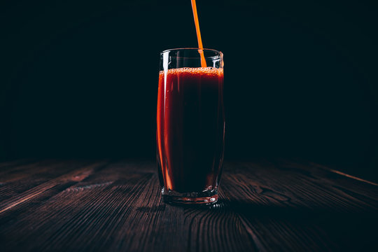 Tomato juice is poured into a full faceted glass on a black background