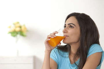 Thoughtful young woman drinking orange juice at home