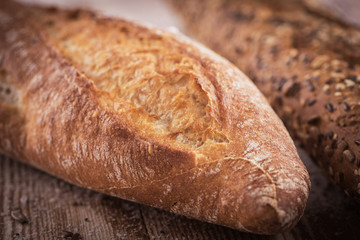 Closeup view of two fresh crunchy baguettes with sunflower seeds and other seeds on the rustic wooden desk