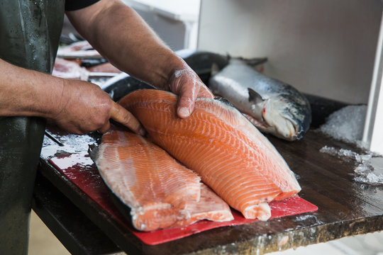 Fishmonger cutting whole salmon fish into fillets