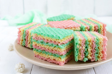 Tasty sweet colorful air waffle cake and cappuccino cup on a white wooden background.