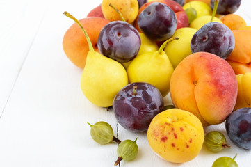 A pile of juicy summer fruits on white wooden background (plums, apricots, pears). Harvest from the garden. A natural source of vitamins.