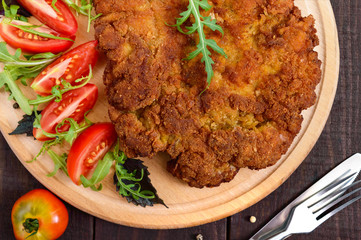 A large Viennese schnitzel  and tomato salad on a cutting board on a dark wooden background. Top view. Close up