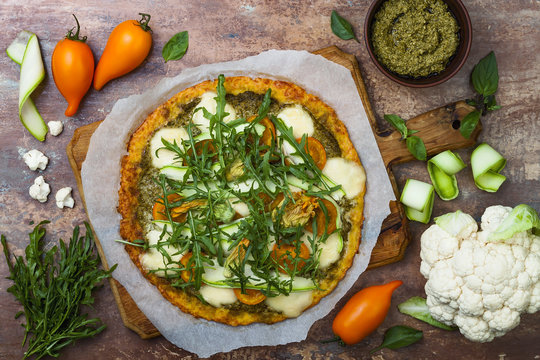 Cauliflower pizza crust with pesto, yellow tomatoes, zucchini, mozzarella cheese and squash blossom.
