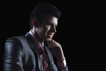 Smiling businessman with hand on chin looking away against black background