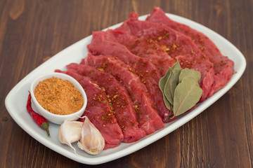 raw meat with herbs on white dish on wooden background