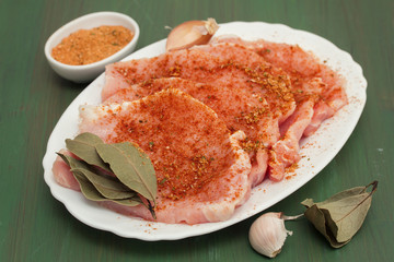 raw pork with herbs on white dish on wooden background