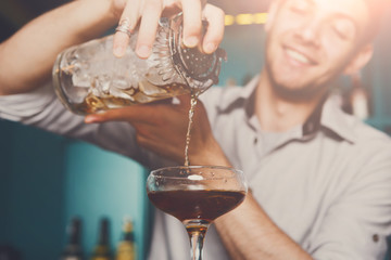 Young bartender pouring cocktail drink into glass