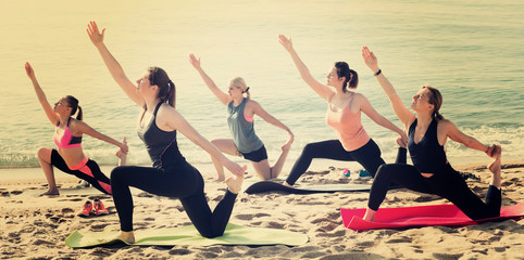 Group of women training hatha yoga on beach