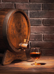 Glass of cognac with barrel on wooden table