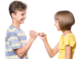 Teen boy and girl on the little finger, hands making promise as a friendship concept. Portrait of happy brother and sister, isolated on white background. 