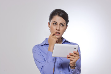 Thoughtful businesswoman with finger in mouth holding digital tablet over gray background