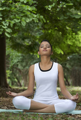 Fototapeta na wymiar Young woman in lotus position meditating in a park 