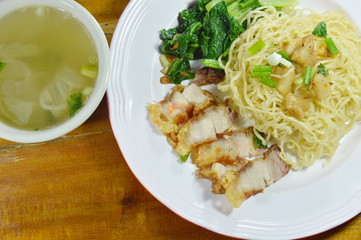 Chinese yellow noodles topping crispy pork on plate with soup