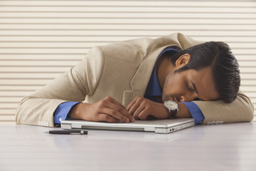 Young businessman sleeping on laptop at desk in office