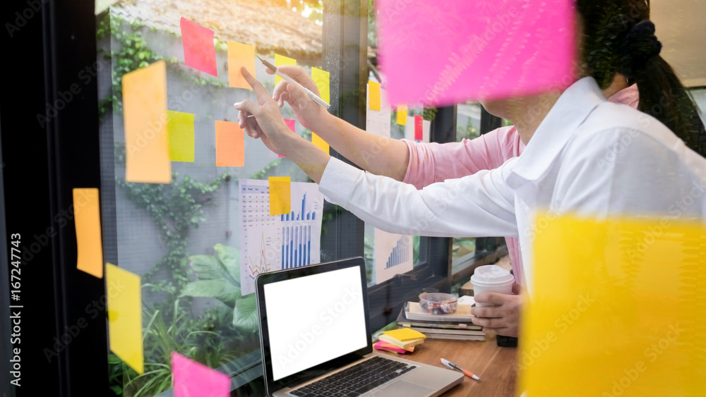 Wall mural business man sticking adhesive notes on glass wall in office and discussing with team