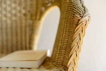 Fototapeta premium Close-up view on the armrest of a rattan armchair with a book laying on the seat.