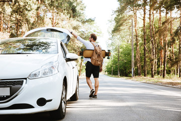 Man with skateboard outdoors standing near car. Looking aside. © Drobot Dean