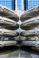 Spiral access ramps of an old decrepit concrete parking lot with a glass office building in the background.