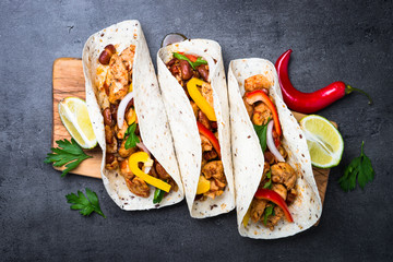 Mexican taco with meat beans and vegetables. Top view on black slate background. 
