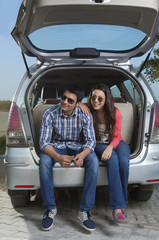 Young man and young woman sitting in the trunk of a car