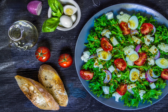 Salad of fresh vegetables and a glass of wine on a black wooden background.