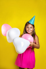 Obraz na płótnie Canvas Studio portrait of a little girl wearing a party hat on her birthday.Happy girl with colorful balloons