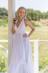 Outdoors portrait of young beautiful blond woman. Female posing in alcove in long white dress.