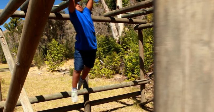 Determined boy climbing horizontal bars during obstacle course
