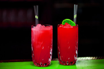 Two red cocktail drinks on black background on green table. Space in background for copy, text, your words