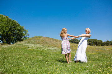 Naklejka na ściany i meble Mother and daughter dancing in a meadow. Young mom and her little daughter holding hands spinnig together.