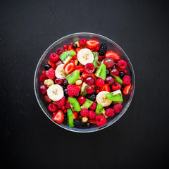 Natural breakfast, fruit salad in glass plate on black table. Flat lay, top view