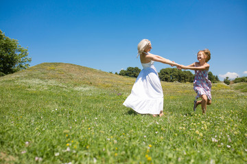 Mother and daughter holding hands, spinning, smiling. Happy woman with her child having fun in a meadow.
