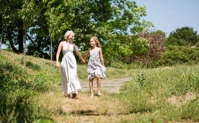 Naklejka na ściany i meble Family walk in the garden, mother and daughter together. Summer vacation, mom and little girl holding hands.