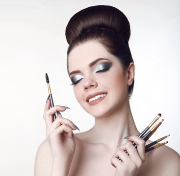 Makeup artist. Pretty teen girl with cute bun hairstyle and fashion beauty makeup, brunette holding brushes in hand isolated on white studio background.