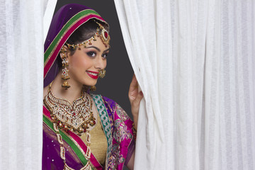 Beautiful Indian bride smiling amidst curtains