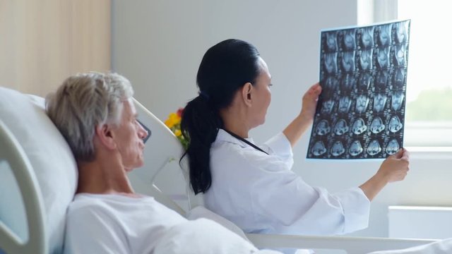 Pleasant female doctor showing x ray scan to her aged patient