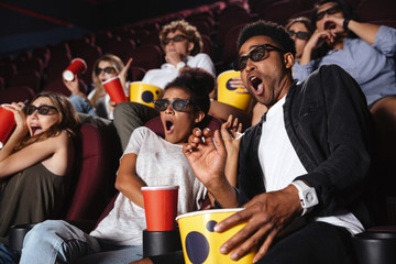 Scared young friends sitting in cinema watch film - obrazy, fototapety, plakaty