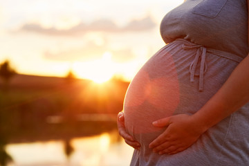Pregnant woman touching her belly at sunset