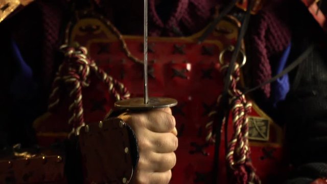 The camera rises from the hands of a samurai in red armor that holds a katana on the face of a samurai in a demon mask, refocus