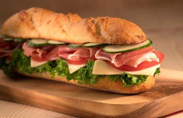 Fresh crispy deli sandwich with prosciutto, cheese, tomatoes, lettuce, cucumbers on a wooden background.Close Up. Healthy concept.