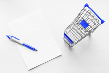 Cart from the grocery store and blank sheet of paper with pen on the white background. Shopping list. Empty shopping trolley. Business ideas and retail trade. Advertising of food products.