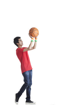 Full length of young boy in casuals aiming basketball over white background 