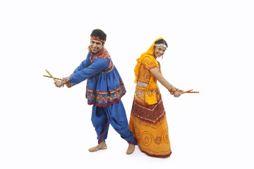 Obraz premium Full length of an Indian couple in traditional wear performing Dandiya Raas over white background