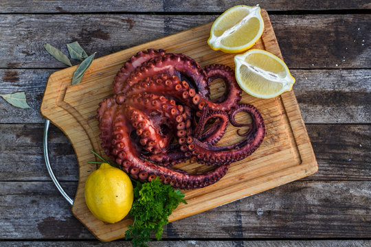 Boiled octopus ready for serve with lemon and parsley on wooden board