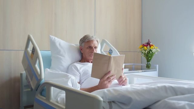 Dolly shot of a thoughtful aged man reading book in a hospital