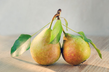  Paired fruit - two pears on one stalk with leaves. With drops of water, lit by the sun on a wooden background. Toned image..