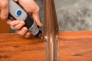 Closeup of a hardworker man drilling a a metallic piece in a wooden piece with his drill, in a gray background, top view