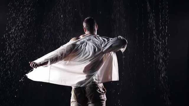muscular male athlete night in the pouring rain removes a large standing with his back to the camera with wet shirt in white. strips sport back