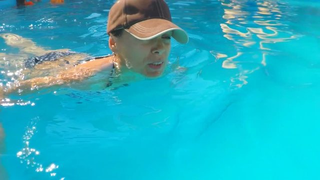 The girl is swimming in the pool. Girl in a baseball cap in the pool.